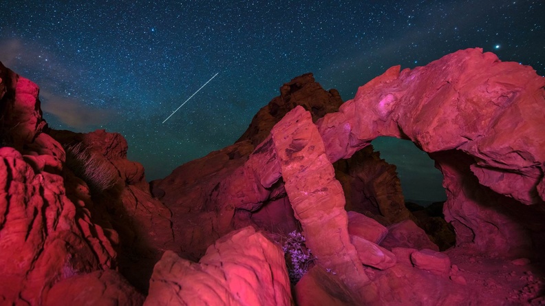 Streak in night sky over rocky arch